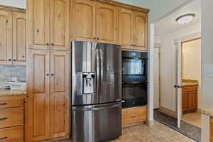 Kitchen with stainless steel fridge, light tile patterned flooring, light stone counters, and tasteful backsplash