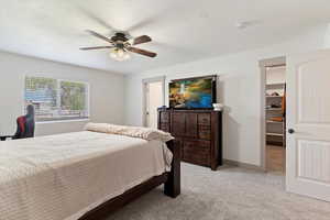 Bedroom with light carpet, a walk in closet, ceiling fan, and baseboards