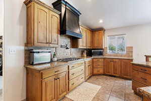 Kitchen featuring custom exhaust hood, stainless steel appliances, backsplash, light stone countertops, and recessed lighting