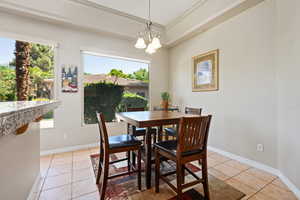 Dining area with light tile patterned floors, healthy amount of natural light, baseboards, ornamental molding, and a chandelier