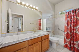 Full bath with tile patterned flooring, shower / bath combination with curtain, toilet, and vanity