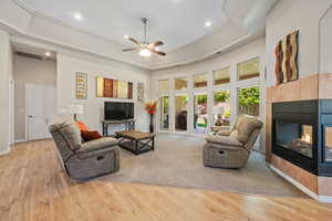 Living area with a fireplace, light wood-type flooring, recessed lighting, ceiling fan, and a tray ceiling