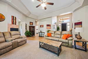 Carpeted living area featuring a towering ceiling, a ceiling fan, arched walkways, a tile fireplace, and a chandelier