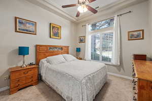 Bedroom with light carpet, baseboards, a ceiling fan, and a raised ceiling