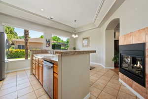 Kitchen featuring stainless steel appliances, light tile patterned floors, a raised ceiling, a sink, and a tile fireplace