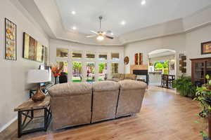 Living area with arched walkways, a ceiling fan, a raised ceiling, recessed lighting, and light wood-style floors