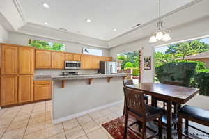 Kitchen with stainless steel appliances, a raised ceiling, healthy amount of natural light, a breakfast bar, and recessed lighting
