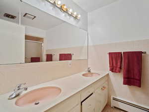 Bathroom featuring a baseboard heating unit, a stall shower, double vanity, and tile walls