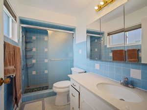 Full bathroom with tile patterned flooring, tile walls, a stall shower, toilet, and vanity