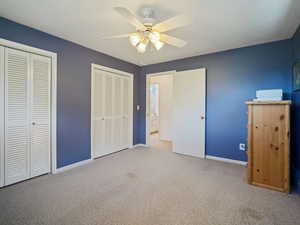 Unfurnished bedroom with two closets, carpet flooring, baseboards, and ceiling fan