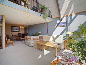 Carpeted living area with a chandelier, beamed ceiling, and high vaulted ceiling