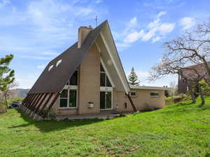 Rear view of house with a patio, a chimney, brick siding, and a lawn