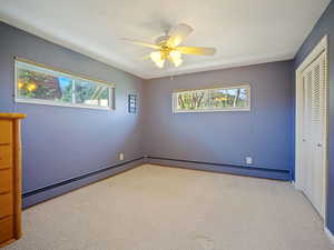 Unfurnished bedroom featuring carpet floors, a closet, a baseboard heating unit, and ceiling fan