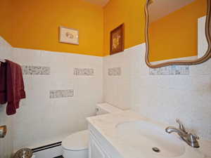 Bathroom with tile walls, a baseboard heating unit, toilet, and vanity