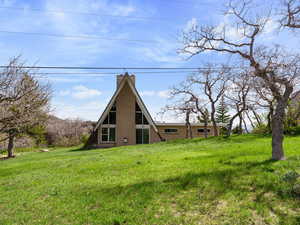 Back of property featuring brick siding, a chimney, and a lawn