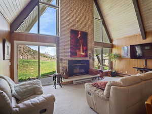 Living area with high vaulted ceiling, wood walls, carpet flooring, a fireplace, and beam ceiling