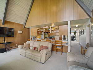 Living area featuring light colored carpet, wood walls, high vaulted ceiling, and beam ceiling
