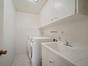 Laundry area with tile walls, washing machine and dryer, and cabinet space
