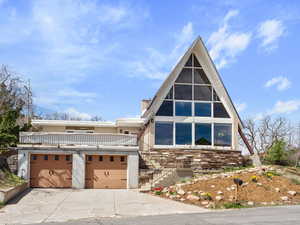 A-frame home with a garage, driveway, stucco siding, and stairway