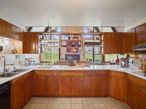 Kitchen featuring black dishwasher, a sink, light countertops, and a brick fireplace