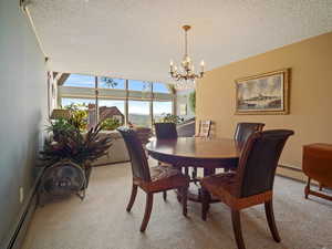 Dining area featuring light colored carpet, a baseboard heating unit, a textured ceiling, and a chandelier