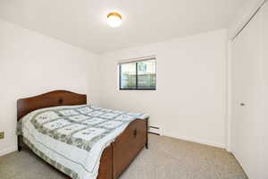 Bedroom with a baseboard heating unit, carpet flooring, baseboards, and a closet