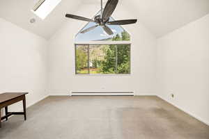 Carpeted spare room featuring baseboard heating, a skylight, baseboards, a ceiling fan, and high vaulted ceiling