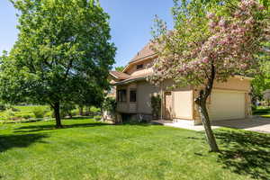 View of property hidden behind natural elements featuring stucco siding, an attached garage, driveway, and a front yard