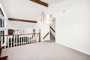 Unfurnished room featuring beam ceiling, high vaulted ceiling, carpet floors, a chandelier, and baseboards