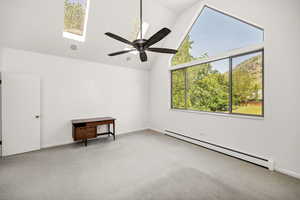 Carpeted empty room with a baseboard radiator, a skylight, a ceiling fan, baseboards, and high vaulted ceiling