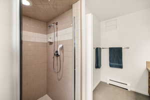 Bathroom with baseboard heating, a tile shower, and baseboards