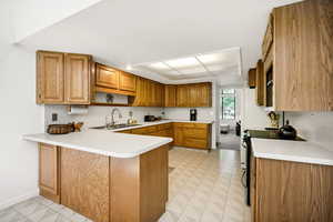 Kitchen featuring a sink, a peninsula, light countertops, and brown cabinetry