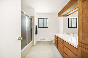 Bathroom with baseboard heating, toilet, vanity, baseboards, and combined bath / shower with glass door