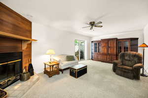 Carpeted living room with a ceiling fan, a fireplace, and baseboards
