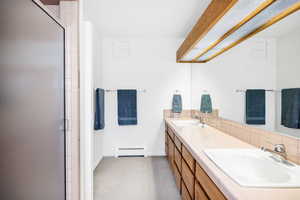 Bathroom with a baseboard radiator, tasteful backsplash, double vanity, a shower with shower door, and baseboards