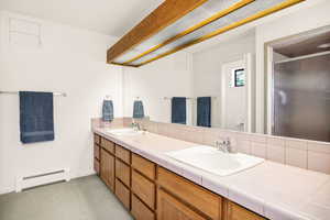 Full bath featuring baseboard heating, tasteful backsplash, a stall shower, and double vanity