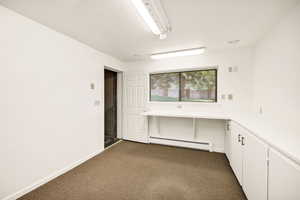 Empty room with a baseboard radiator, dark colored carpet, and baseboards