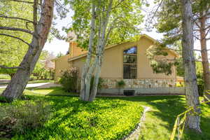 View of property exterior with stone siding, stucco siding, and a lawn