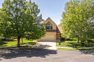 View of property hidden behind natural elements with an attached garage, stucco siding, stone siding, concrete driveway, and a front lawn