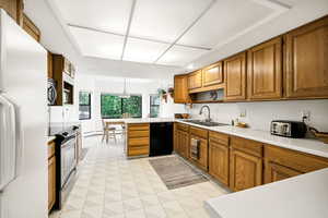 Kitchen featuring freestanding refrigerator, stainless steel electric stove, dishwasher, a sink, and brown cabinets