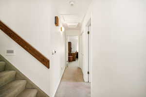 Hall featuring light colored carpet, attic access, stairway, and baseboards