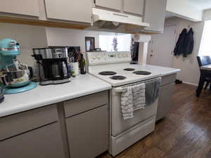 Kitchen featuring white electric range oven, under cabinet range hood, dark wood finished floors, light countertops, and gray cabinetry