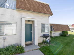 Doorway to property featuring a shingled roof, mansard roof, and a lawn