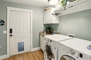 Laundry area featuring washing machine and clothes dryer, cabinet space, light wood finished floors, and baseboards