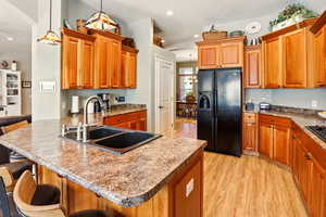 Kitchen featuring black fridge with ice dispenser, a sink, light wood-style floors, a peninsula, and a kitchen bar