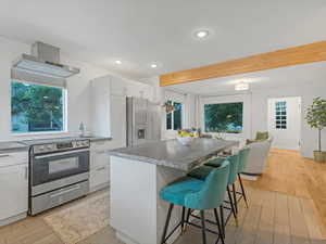 Kitchen featuring appliances with stainless steel finishes, wall chimney exhaust hood, a breakfast bar area, light wood-type flooring, and a center island