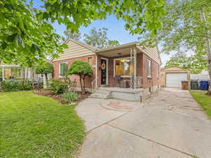 View of front of property with brick siding, an outdoor structure, covered porch, a front lawn, and concrete driveway