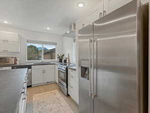 Kitchen featuring appliances with stainless steel finishes, a sink, wall chimney range hood, recessed lighting, and white cabinetry