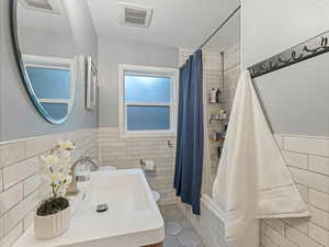 Full bath featuring tile walls, tile patterned floors, curtained shower, and wainscoting