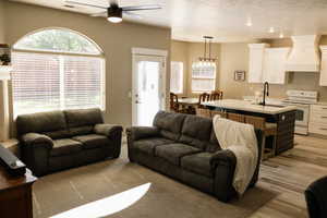 Living room with a ceiling fan, light wood-style floors, a textured ceiling, and a chandelier
